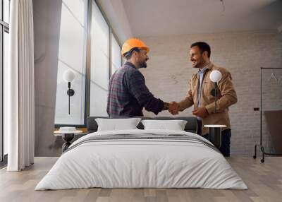 Happy man shaking hands with construction site worker at his renovating home. Wall mural