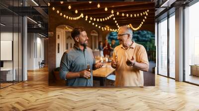 Happy man talks to his senior father while drinking beer together on patio. Wall mural