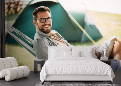 Happy man uses smartphone and laptop while camping in nature and looking at camera. Wall mural