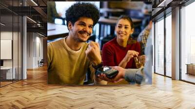 Happy man using smart watch while making contactless payment to waiter in a pub. Wall mural