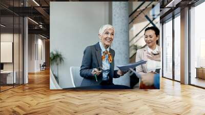 Happy mature businesswoman and her team communicating during business meeting in the office. Wall mural