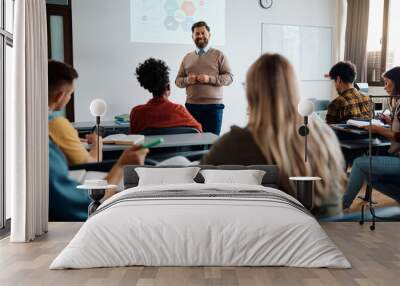 Happy mature teacher talks to his students while holding presentation in lecture hall. Wall mural