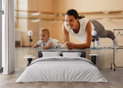 Happy mother with a baby doing plank exercise in health club. Wall mural