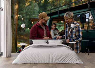 Happy parents cooking during family camping trip in woods. Wall mural