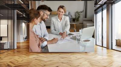 Happy real estate agent showing to a couple where to sign the contract. Wall mural