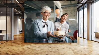 Happy senior businesswoman carries Birthday cake on surprise party in the office. Wall mural