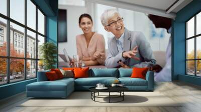 Happy senior CEO using laptop during meeting with coworkers in office. Wall mural