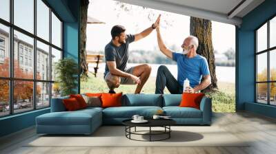 Happy senor athlete and his son greet with high-five after sports training in nature. Wall mural