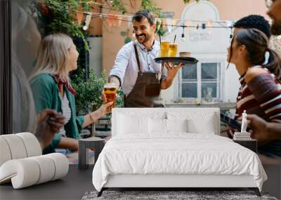 Happy waiter serving drinks to group of guests in cafe. Wall mural