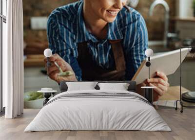 Happy woman following recipe on touchpad while making bruschetta in the kitchen. Wall mural