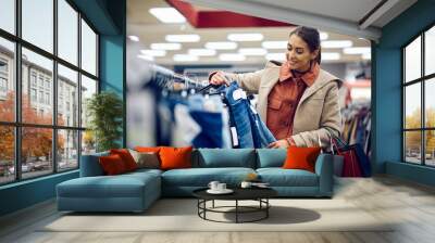 Happy woman looking for jeans while shopping at clothing store. Wall mural