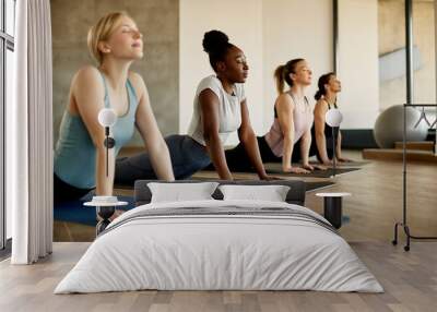 Multi-ethnic group of athletic women doing stretching exercise on Yoga class at health club. Wall mural