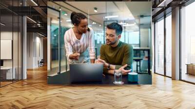 Multiracial colleagues talk while working on laptop in office. Wall mural