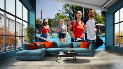 Multiracial group of happy athletes leaving court after playing mixed doubles in paddle tennis. Wall mural