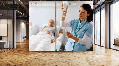 Nurse practitioner checking IV drip of senior patient at hospital ward. Wall mural