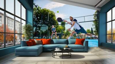 Paddle tennis player making an effort to while hitting ball during match on outdoor court. Wall mural