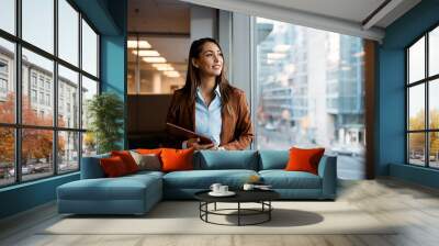 Pensive businesswoman with touchpad looking through window while working in office. Wall mural