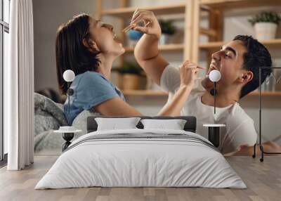 Playful couple feeding each other with a cookie in bedroom. Wall mural