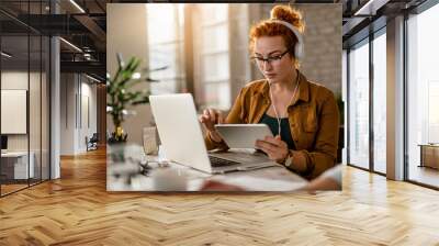 Redhead businesswoman with headphones working on touchpad in the office. Wall mural