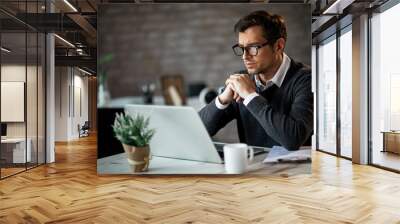 Serious businessman reading something on laptop while working in the office. Wall mural