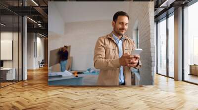 Smiling man using mobile phone during construction works at his house. Wall mural