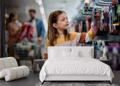 Smiling schoolgirl choosing products at school supplies section in supermarket. Wall mural