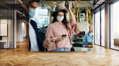 Woman with protective face mask texting on mobile phone while commuting by bus. Wall mural