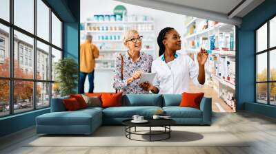 Young black pharmacist assists senior woman in buying medicine in pharmacy. Wall mural