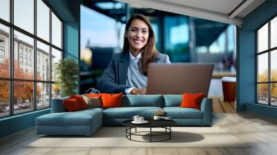 Young businesswoman surfing the net on laptop at train station cafe and looking at camera. Wall mural