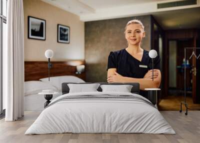 Young chambermaid standing with arms crossed in hotel room and looking at camera. Wall mural