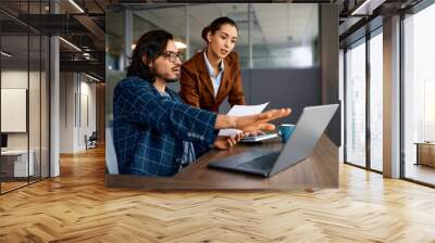 Young entrepreneurs cooperating while working on laptop in office. Wall mural