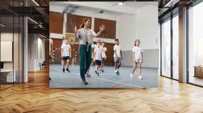 Young female coach has PE class with group of elementary students at school gym. Wall mural