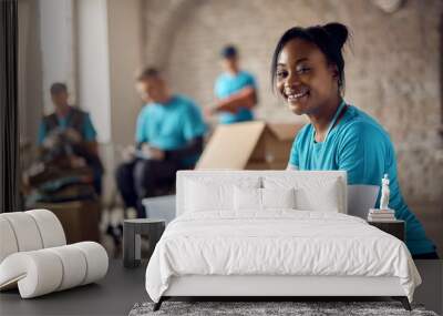 Young happy black woman volunteering at humanitarian aid center and looking at camera. Wall mural