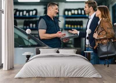 Young happy couple talking to car mechanic in auto repair shop. Wall mural