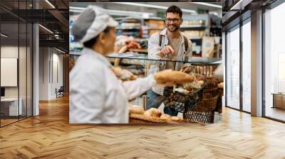 Young happy man buying bread in supermarket bakery. Wall mural