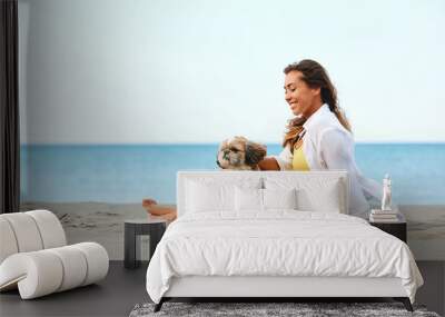 Young happy woman spending summer day on beach with her dog. Wall mural