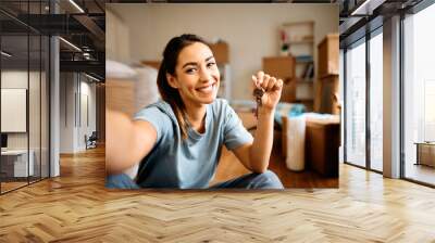 Young happy woman takes selfie while holding key of her new apartment and looking at camera. Wall mural