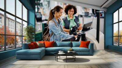 Young happy woman using self-service checkout with help of supermarket worker. Wall mural