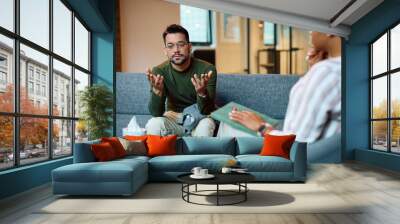 Young man talks during session with mental health therapist in office. Wall mural