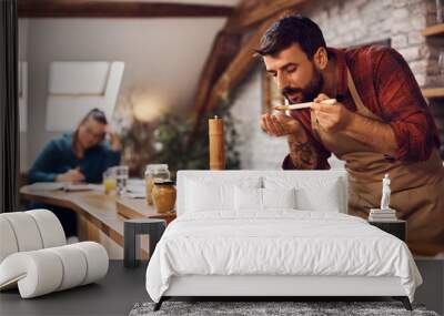 Young man tasting food while cooking in the kitchen. Wall mural