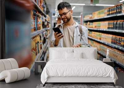 Young man using cell phone while shopping in supermarket. Wall mural