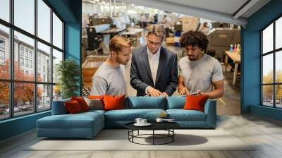 Young metal workers cooperating with their manager while reading reports in a factory. Wall mural