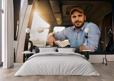 Young truck driver behind steering wheel in vehicle cabin looking at camera. Wall mural