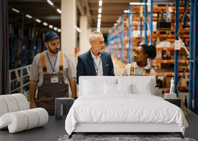 Young warehouse workers talk to their manager while walking through storage compartment. Wall mural