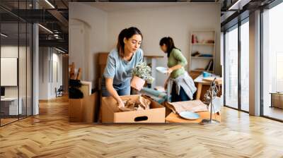 Young woman and her friend packing their belongings while preparing to move out of apartment. Wall mural