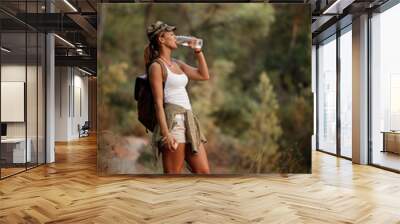 Young woman drinking water while hiking through nature. Wall mural