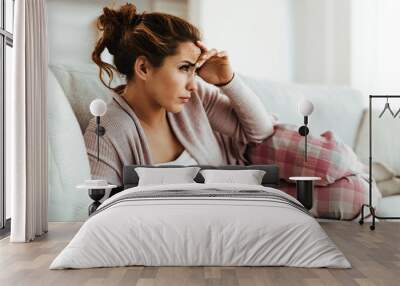 Young woman having headache while reading book on the sofa at home. Wall mural