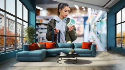 Young woman reads product label while buying diary product in supermarket. Wall mural