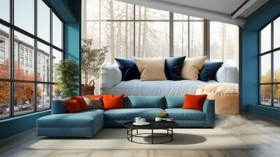 A cozy and minimalistic living room with large windows, an indoor plant in a woven basket, a plush light blue couch with beige and blue throw pillows, a tan pouffe, warm wooden floors, natural light f Wall mural