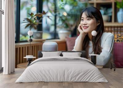 Asian woman sitting with a smart speaker on a table in a cozy cafe. Smart home assistant with Ai. Voice controlled device. Modern and future technology. Home automation concept.  Wall mural